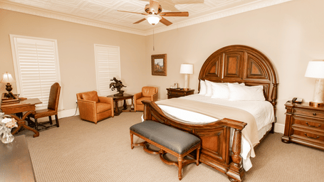 Bedroom with wooden bed and leather seating at The Grand Hotel & Ballroom, McKinney.