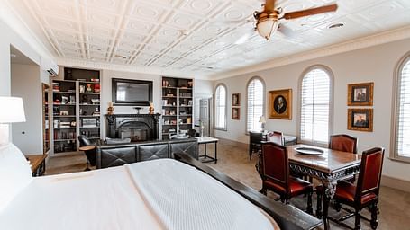 A large bedroom featuring a bookshelf with books, a cosy seating area, and a comfortable bed, providing a relaxing environment - The Grand Hotel & Ballroom, McKinney
