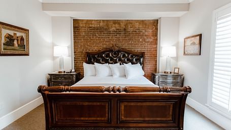  A classic bedroom with dark wood furniture, a large bed, and soft, natural lighting from the window, providing a serene retreat - The Grand Hotel & Ballroom, McKinney