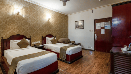 A hotel bedroom with 2 separate single beds, wooden flooring, and patterned wallpaper at The Lindsay, Kolkata.
