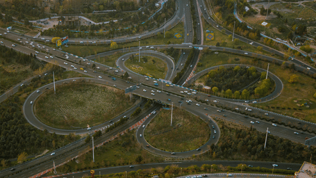 An aerial view captures a large, complex multi-level highway interchange surrounded by green landscape.