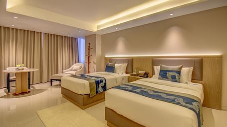 Side view of a well-lit Premium Twin room at The SSK Solitaire Boutique Hotel & Spa, Gangapur Road - Nashik featuring a twin  bed, two armchairs, a small table, and a work desk with a chair.