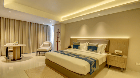 Overview of a well-lit Deluxe King room at The SSK Solitaire Boutique Hotel & Spa, Gangapur Road - Nashik featuring a king size  bed, two armchairs, a small table, and a work desk with a chair.