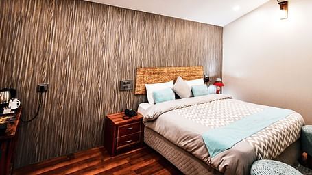 image of the standard room featuring a double bed in the corner with wooden flooring - The Tattva Boutique Resort