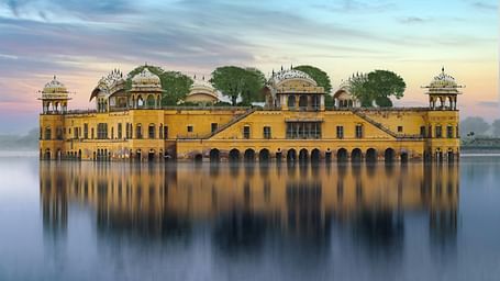 The Jal Mahal, a yellow sandstone palace, appears to float serenely on the still waters of Man Sagar Lake in Jaipur, under a soft, twilight sky.