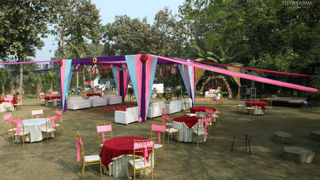 An outdoor wedding venue with round tables covered in red tablecloths, white chairs, and draped canopies for shade at at Tisya Farms.