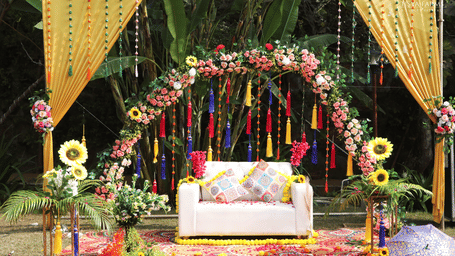 A wedding stage with a white sofa under a floral arch, decorated with hanging tassels and sunflowers at Tisya Farms.