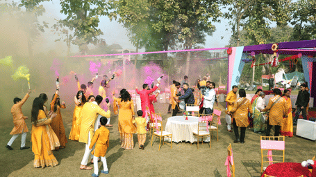 Guests playing with colored powder at an outdoor event setup with tables and canopy at Tisya Farms, Gurgaon.
