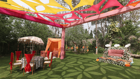 Outdoor wedding setup at Tisya Farms, Gurgaon with red chairs, and floral seating area under colourful drapes.