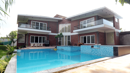 View of villa exterior with a swimming pool and patio area at Tisya Farms, Gurgaon.