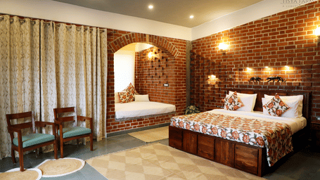 A bedroom at Tisya Farms, Gurgaon with a double bed, chairs, brick walls, curtains, and overhead lighting.