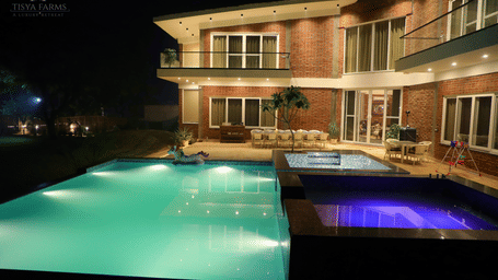 A night view of a farmhouse with an illuminated swimming pool in front at Tisya Farms, Gurgaon.