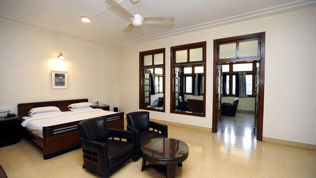 The Osho Suite with a large bed, dark wood armchair seating area, and tall glass doors leading to another space | Trance Sunderban Resort
