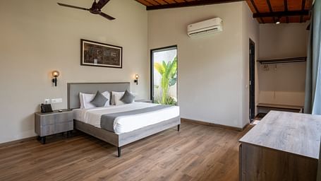  Ananta Garden Villa bedroom at Trance Veechika Resort: a spacious room with a bed, large window, fan, and wooden floor.