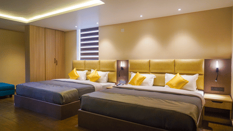 Room with two double beds, yellow cushions, padded headboards, and warm recessed lighting at Trident The Boutique Hotel, Ooty.