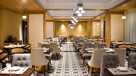 A restaurant interior with patterned tile floor, upholstered chairs, set tables, hanging pendant lights, and decorative ceiling panels - Urban Suites by BluSalzz, Jaipur