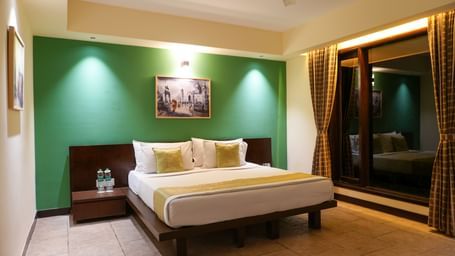 Bedroom in the Retreat Villa at Vedic Village Spa Resort with a double bed, wooden headrest, ceiling fan, and a large wall-to-wall window offering a night-time view of the outdoors.