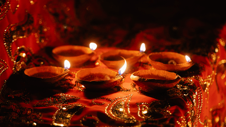 Traditional terracotta oil lamps glowing warmly against a rich red ornate fabric backdrop.