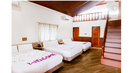 A spacious bedroom with multiple beds and a wooden staircase, featuring pink petals on the nearest bed spelling WELCOME | Vintage Trails By Ilara
