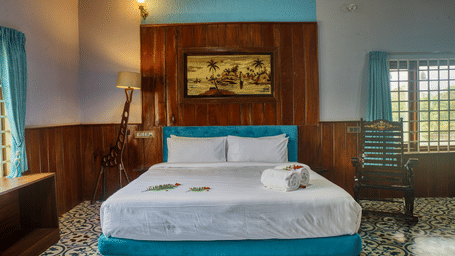 A hotel bedroom featuring a large bed with white linens and a blue bed frame, a wooden headboard, and a window with light filtering in.