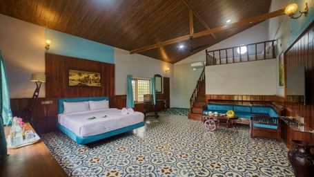 The interior of a bedroom or common area with a patterned tiled floor, a large bed with a light blue bedspread, and ceiling, and a seating area with a sofa. - Vintage Trails by Ilara