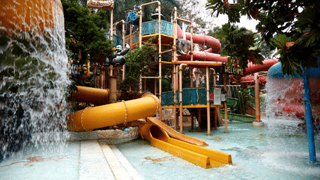 A vibrant scene at Water Kingdom in Mumbai, showcasing a yellow water slide, lagoon and various water play structures.