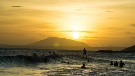 An overview of Mui Ne Beach with people swimming and surfing, and the sun setting in the background.
