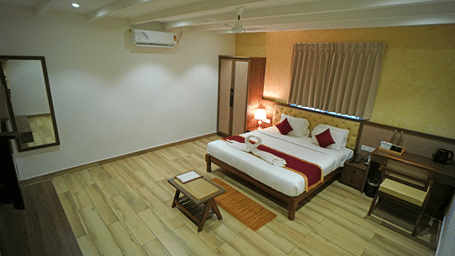 A room at WOW Naturefull Resorts, Yercaud, with a large bed, spreads, pillows, an air-conditioner, a table, and a mirror.