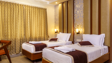A bedroom at Wyt Hotels, Rameswaram featuring twin beds, a chair, and bedside tables with lamps for both beds.