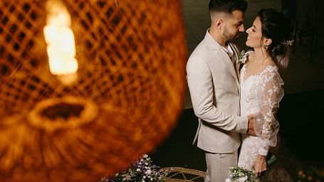 a couple close to each other dressed in western wedding attire with a blurry bamboo lamp in front of them