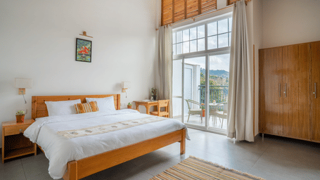 A wide shot of a Ziran Retreat bedroom with a large bed, a wooden bedside table, and large glass doors open to a balcony with a scenic view.