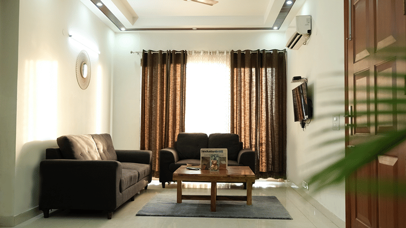 Living room of Lime Tree Hotels & Service Apartment Private Limited featuring a brown sofa, gold curtains, and a coffee table.