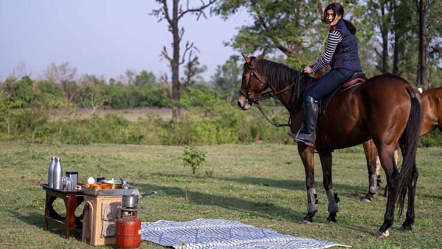 A woman on a horse back near a picnic setup surrounded by lush greenery
