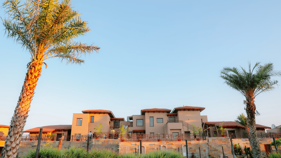 Several resort buildings with palm trees under a clear blue sky at Aamaghati Wildlife Resort.