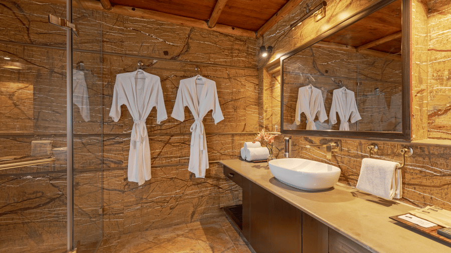 A stylish bathroom with a basin, large mirror, and bathrobes hanging at Aamaghati Wildlife Resort.