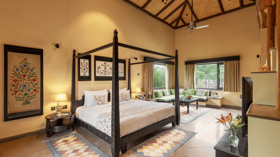 A luxurious bedroom with a dark wood four-poster bed and vibrant rug at Aamaghati Wildlife Resort.