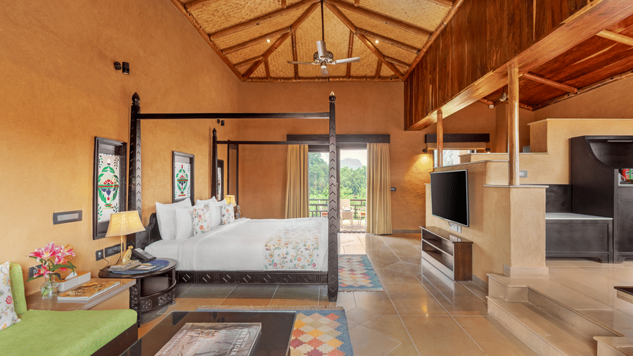 A wide view of a spacious bedroom with a four-poster bed and seating at Aamaghati Wildlife Resort.