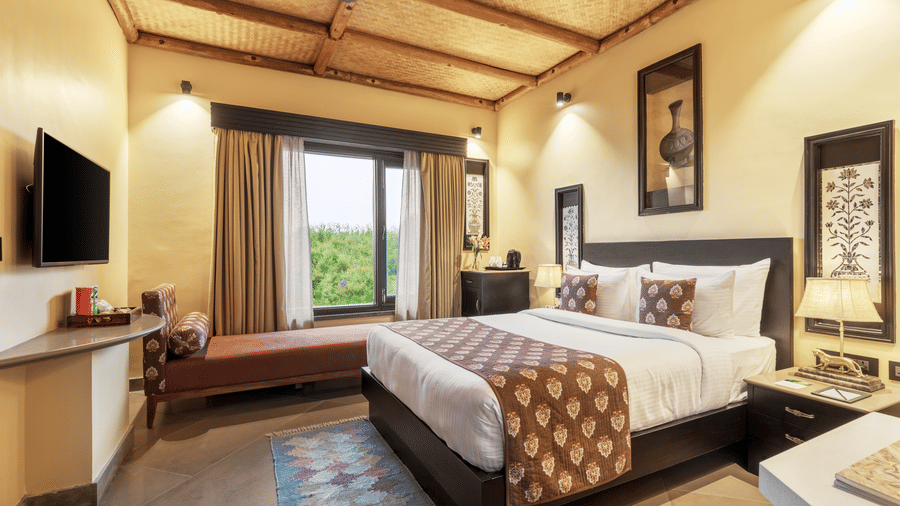 A spacious bedroom with a large bed and an adjoining sitting area at Aamaghati Wildlife Resort.