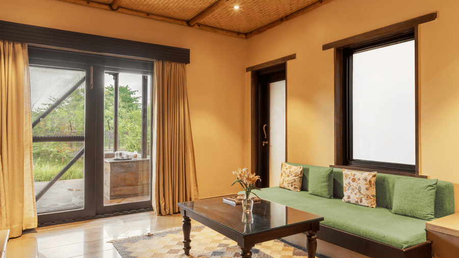 A comfortable living room with a green sofa and a view to the outside at Aamaghati Wildlife Resort.