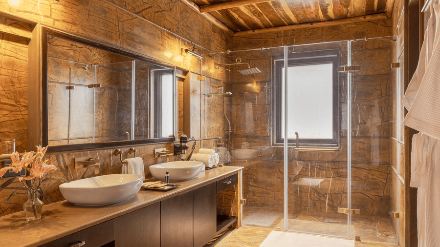 A spacious bathroom with twin sinks, a large mirror, and a shower at Aamaghati Wildlife Resort.