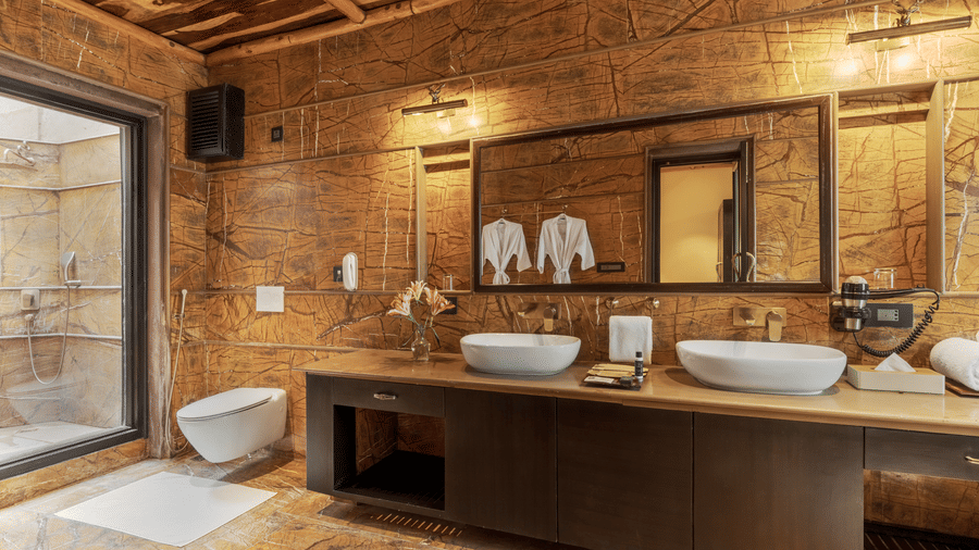 A modern bathroom with a stone feature wall and double vanity at Aamaghati Wildlife Resort.