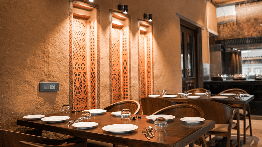 A dining table near a wall with traditional art and warm lighting at Aamaghati Wildlife Resort.