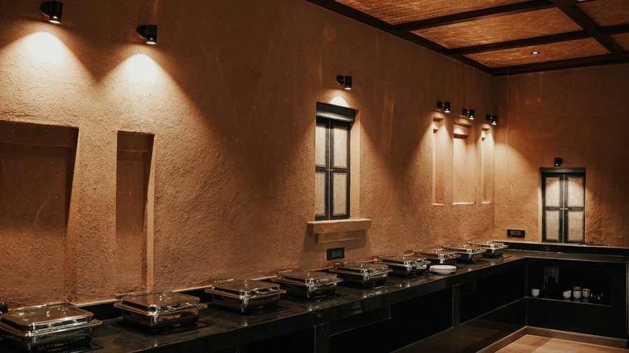 A buffet counter area with serving dishes under warm lighting at Aamaghati Wildlife Resort.
