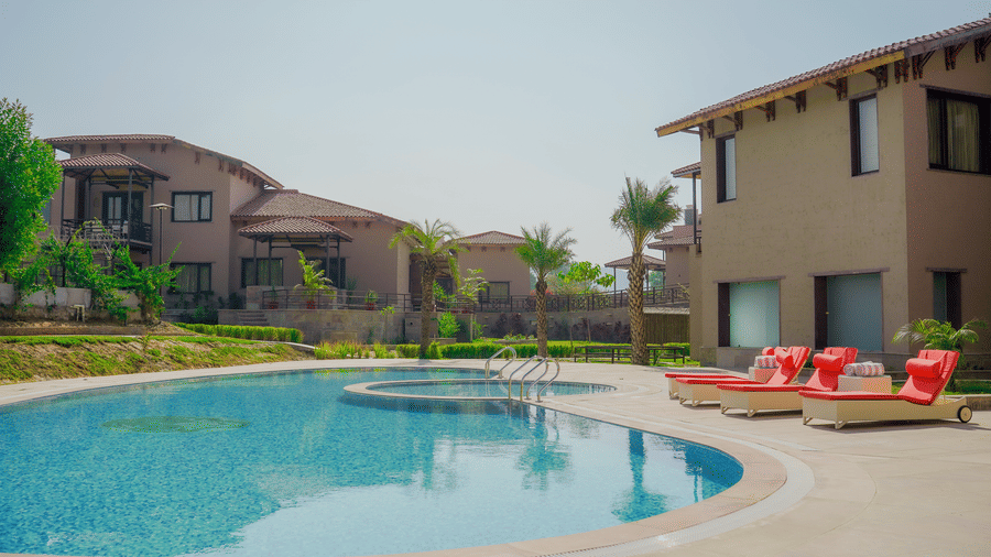 A resort swimming pool surrounded by comfortable orange sun loungers at Aamaghati Wildlife Resort.