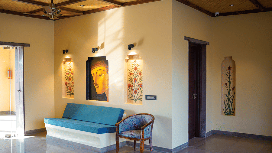 A spacious lounge area with a blue sofa and cultural artwork at Aamaghati Wildlife Resort.