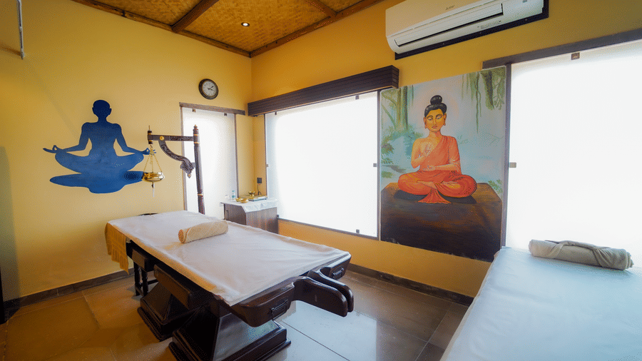 A wide view of a spa treatment room with wooden massage beds and wall art at Aamaghati Wildlife Resort.