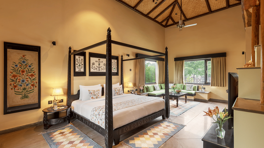 A luxurious bedroom with a dark wood four-poster bed and vibrant rug at Aamaghati Wildlife Resort