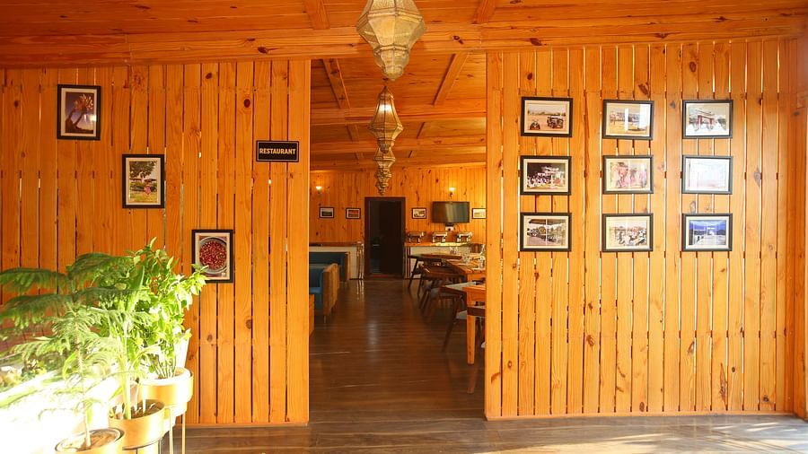 Entryway to the dining area featuring wall-mounted photo frames, a hanging lamp, and potted plants on the side at Aanandam Resort & Spa