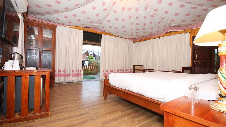 Spacious Luxury Wooden Tent featuring a bed with a bedside lamp and a wall-mounted TV at Aanandam Resort & Spa