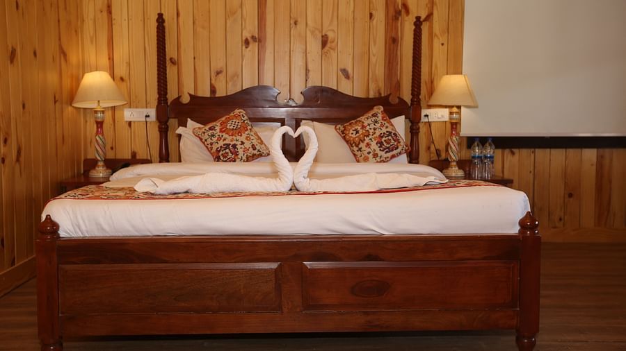 Front view of the king-sized bed, with bedside bedlights and decorative towels on it at Aanandam Resort & Spa